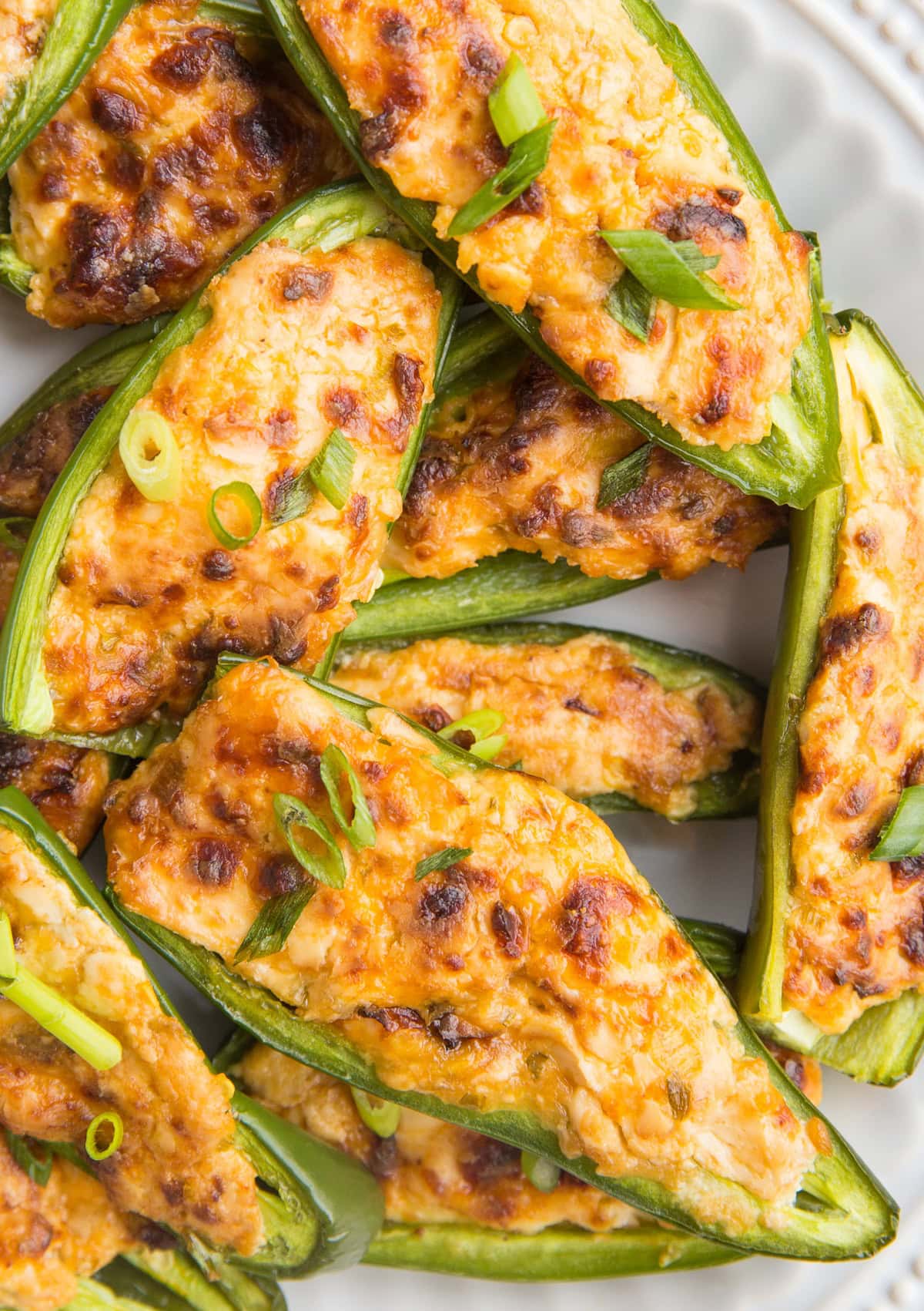 Close up top down image of halved jalapenos stuffed with cream cheese and melted cheese sprinkled with green onions. Ready to serve.