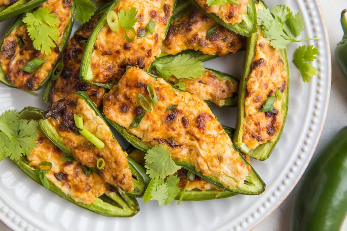 Plate full of cream cheese stuffed jalapeno peppers with fresh cilantro on top.