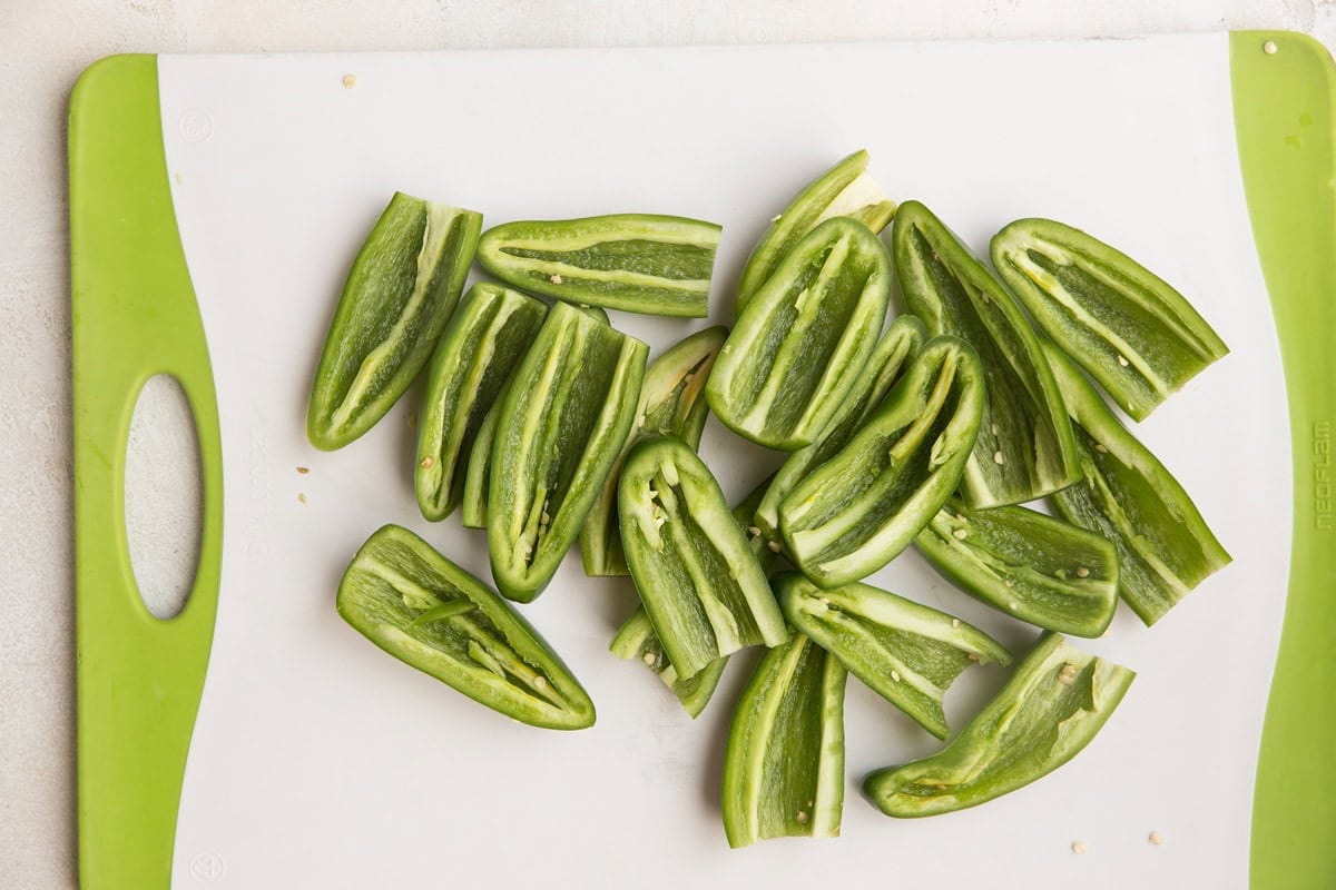 White and green cutting board with fresh Jalapeños sliced in half with the tops and seeds removed.