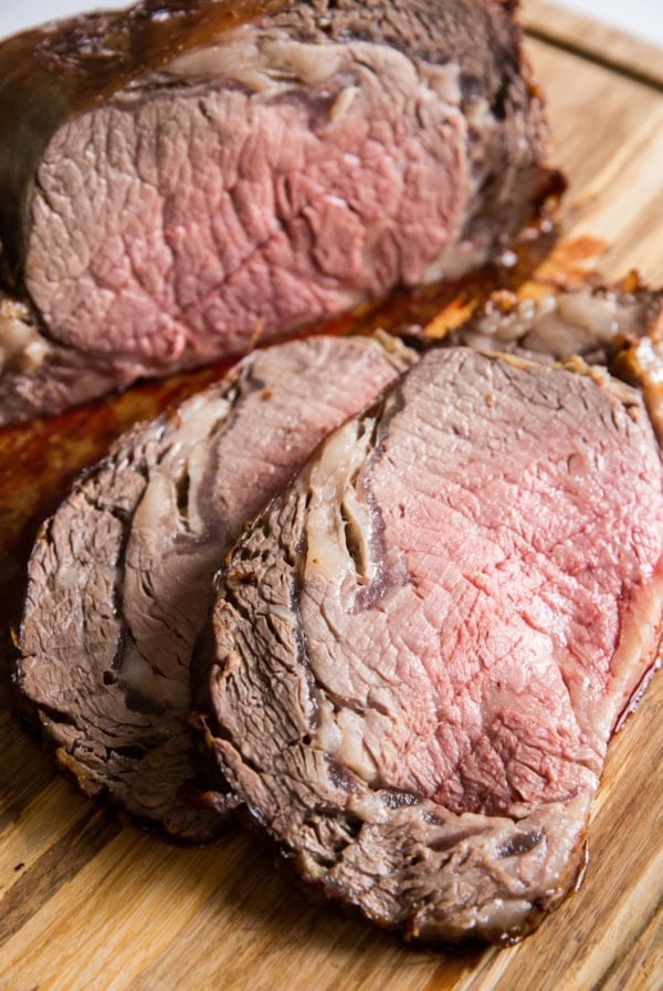 Prime rib cut into individual steaks on a wooden cutting board with juices seeping out.
