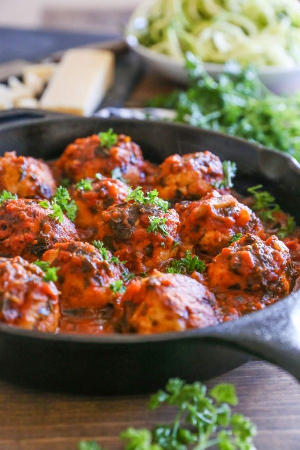 Cast iron skillet full of turkey meatballs slathered in tomato sauce. Fresh parsley to the side and parmesan cheese in the background.