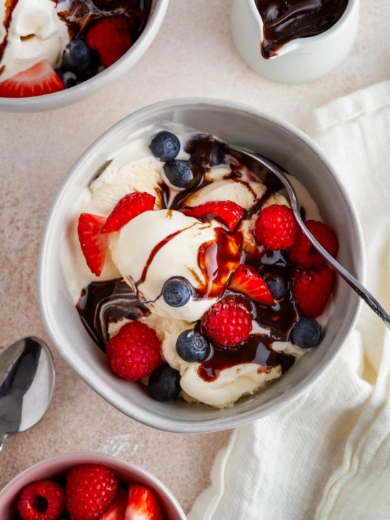 Homemade vanilla ice cream in a bowl with fresh berries and chocolate sauce, ready to eat