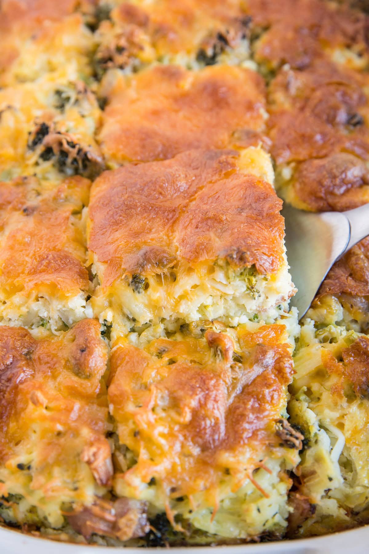 Broccoli Cheddar Egg Casserole with Hashbrowns in a casserole dish with a spatula starting to pull out a piece.