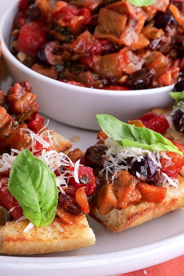 Toasted baguette with eggplant caponata topped with parmesan cheese and fresh basil, ready to serve.
