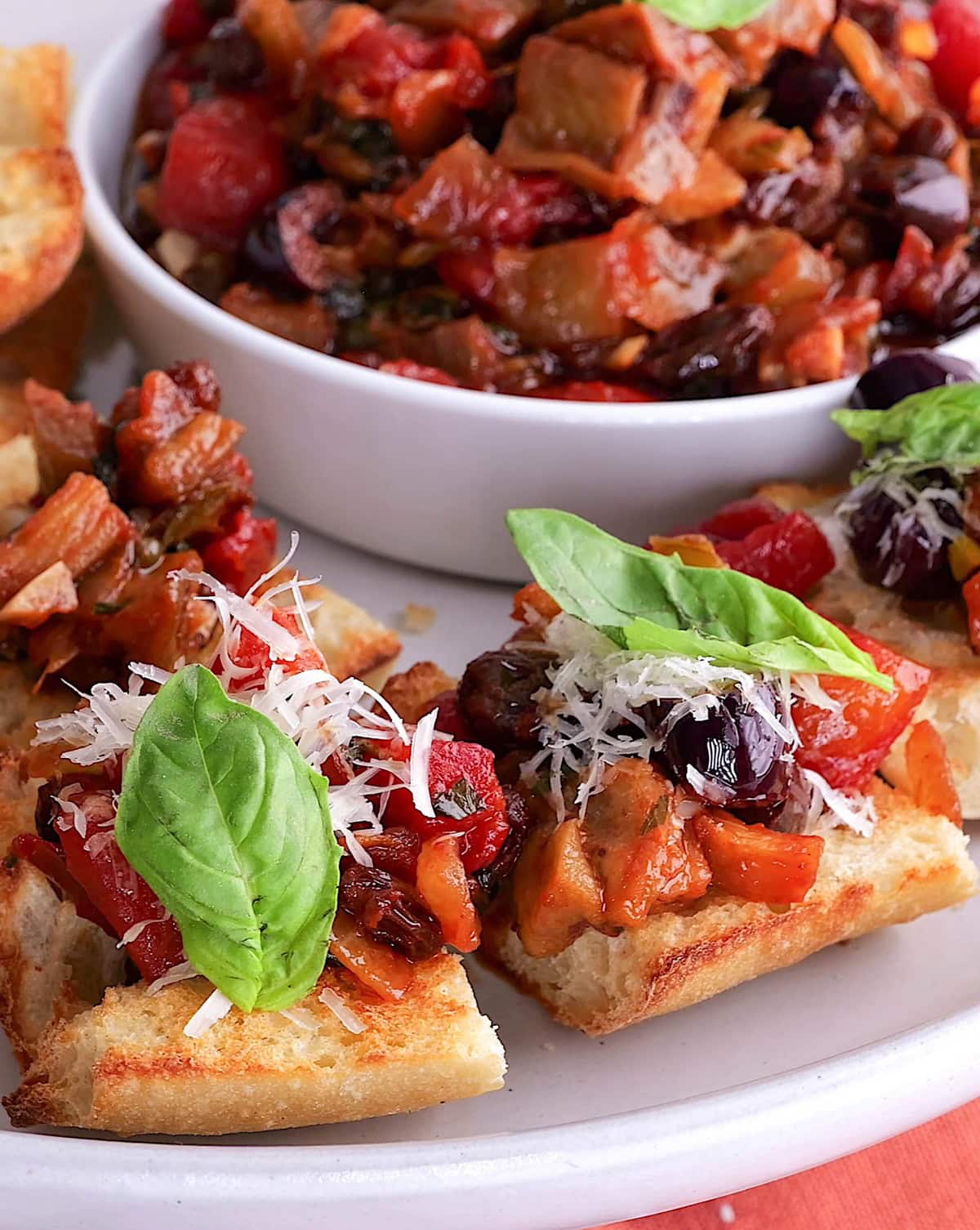 Toasted baguette with eggplant caponata topped with parmesan cheese and fresh basil, ready to serve.