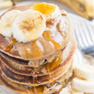 Stack of oatmeal banana pancakes on a plate with almond butter, honey, and sliced bananas on top.