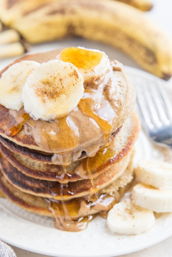 Stack of oatmeal banana pancakes on a plate with almond butter, honey, and sliced bananas on top.