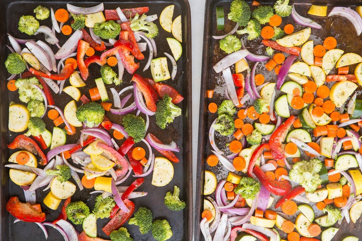 Two large baking sheets with vegetables spread on them in a single layer, ready to go into the oven.