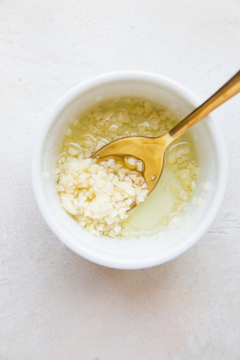 Fresh minced garlic and avocado oil mixed together in a small white bowl.