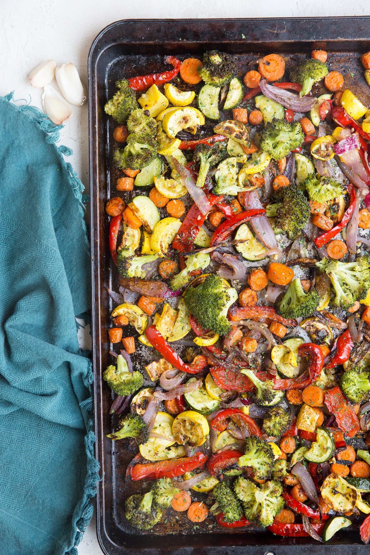 Garlic herb roasted vegetables on a large sheet pan, fresh out of the oven with a blue napkin to the side.