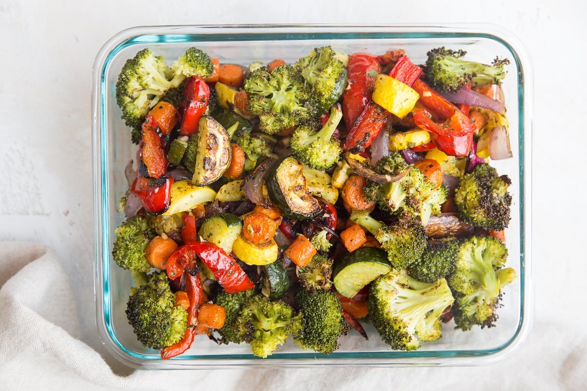 Meal prep roasted vegetables in a large glass container, to be stored in the refrigerator.