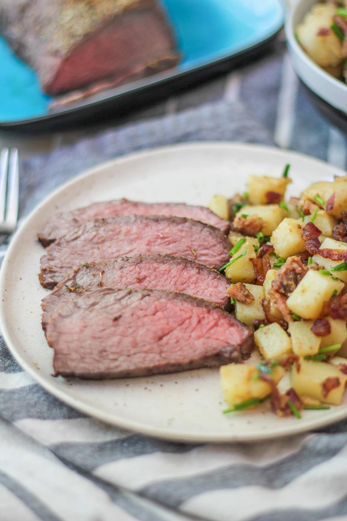 Slices of tri tip on a plate with German potato salad next to the meat. Ready to serve.