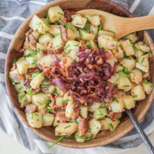 Large wooden bowl full of German potato salad with caramelized onions on top, ready to be mixed in.