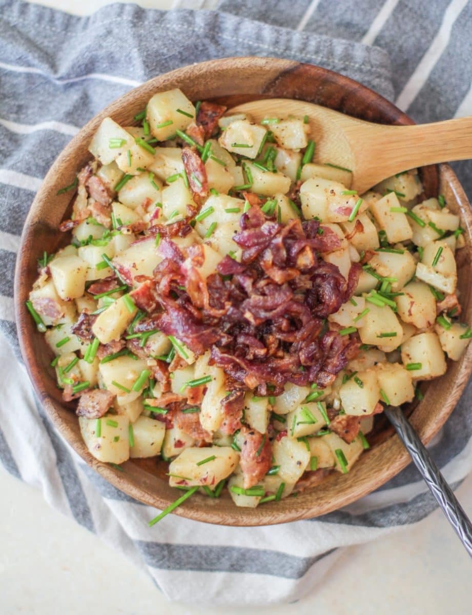 Large wooden bowl full of German potato salad with caramelized onions on top, ready to be mixed in.