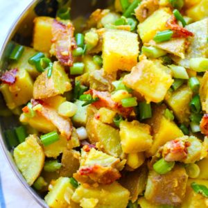 Large stainless steel bowl full of German Sweet Potato salad with bacon and green onions.
