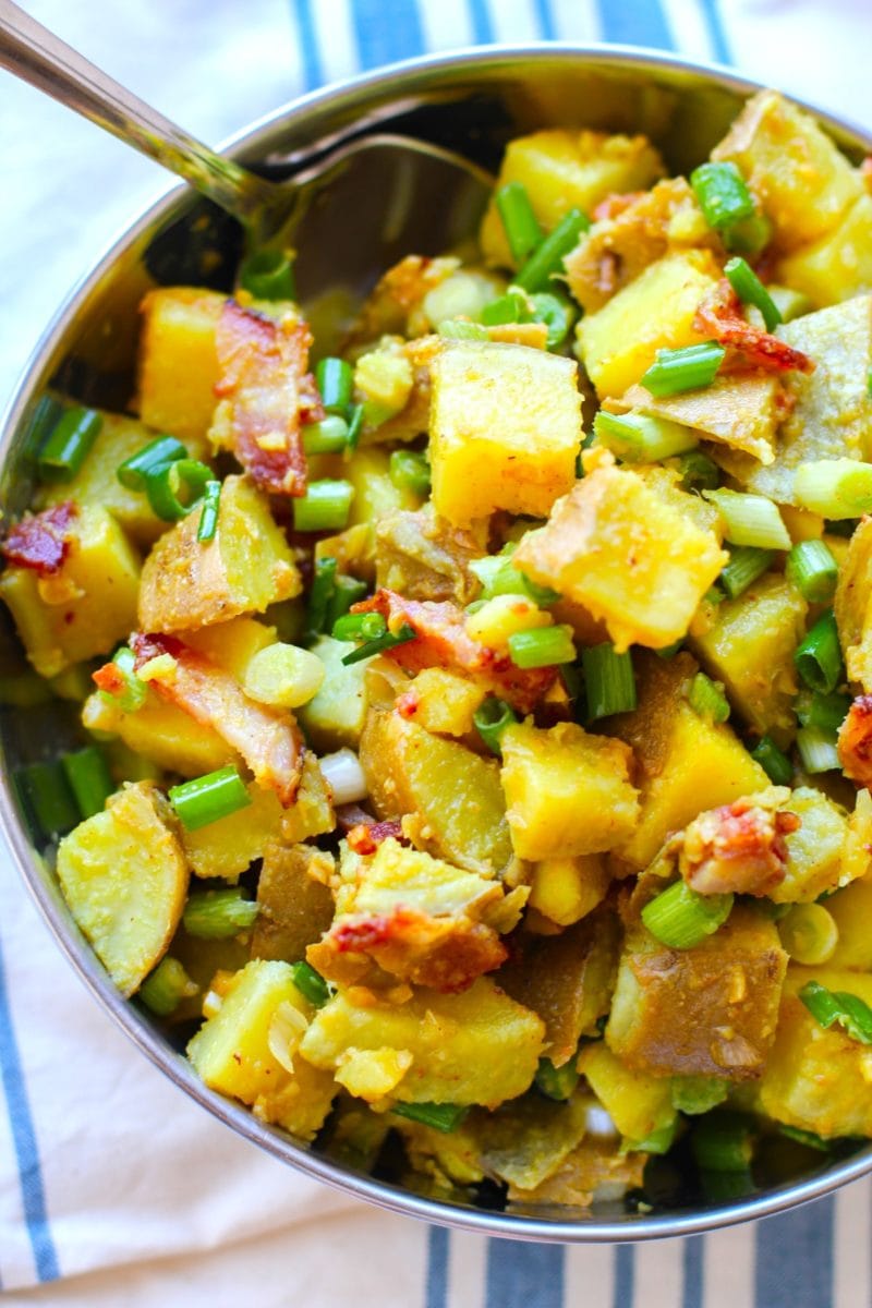 Large stainless steel bowl full of German Sweet Potato salad with bacon and green onions.