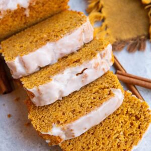 Pumpkin spice bread cut into slices with a glaze on top, cinnamon sticks and a golden napkin in the background.