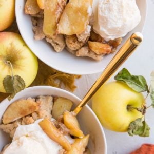 Dairy-Free Gluten-Free Apple Cobbler in two white bowls with vanilla ice cream on top and fresh apples to the side.