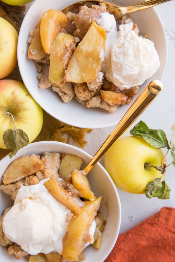 Dairy-Free Gluten-Free Apple Cobbler in two white bowls with vanilla ice cream on top and fresh apples to the side.