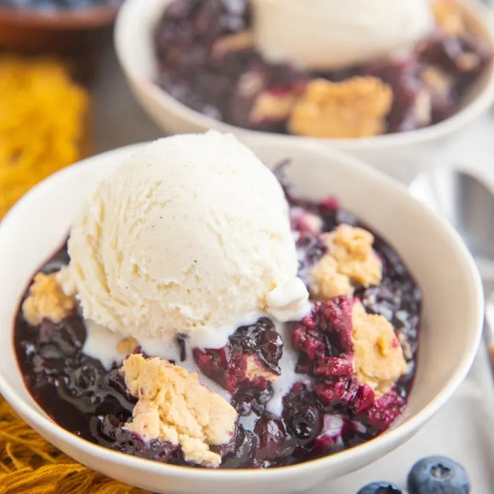 Two white bowls of blueberry cobbler with scoops of ice cream on top.