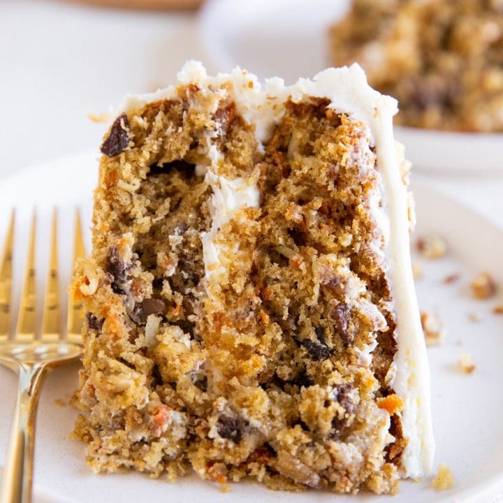 Thick slice of carrot cake on a white plate with a gold fork.