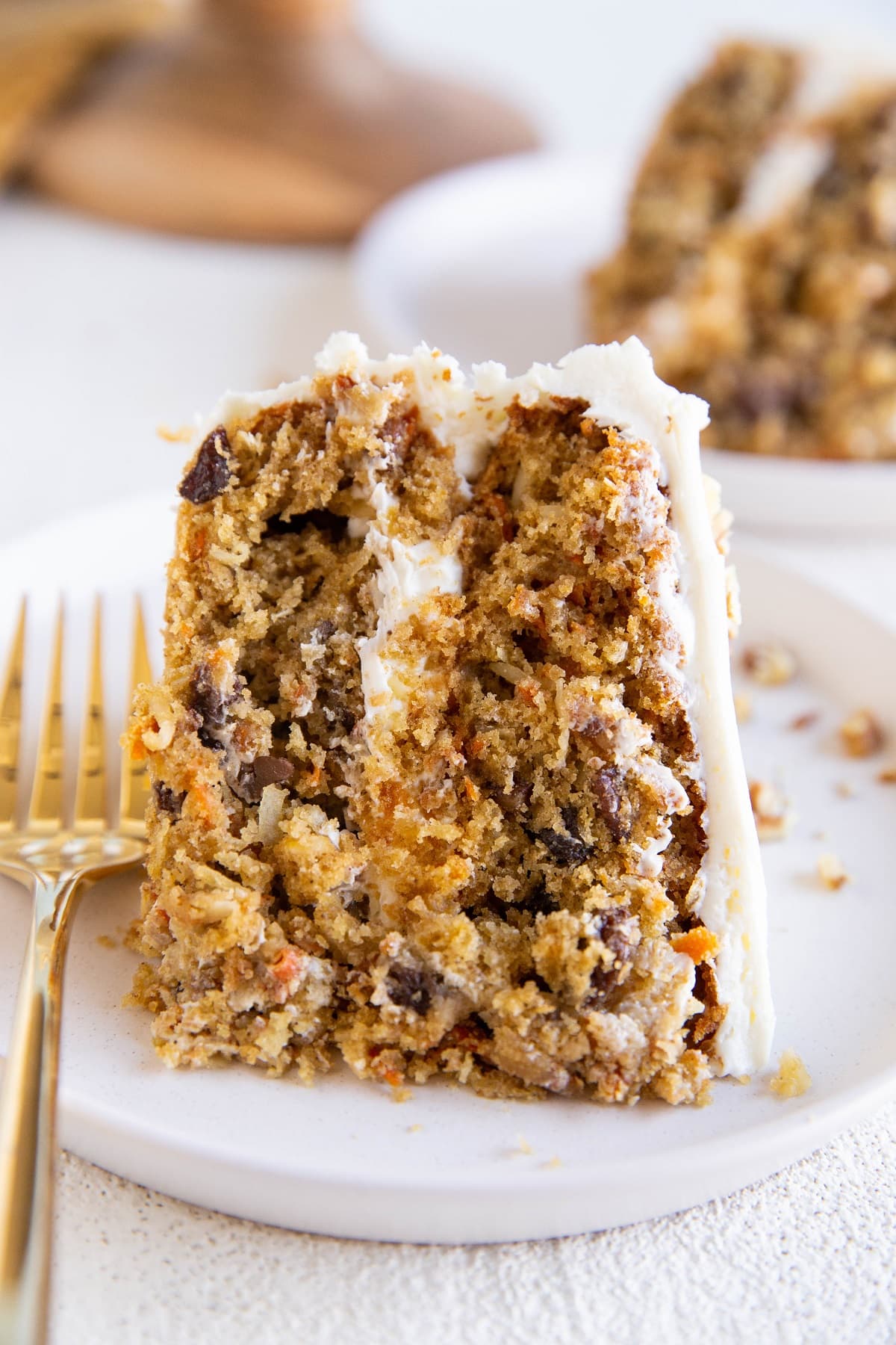 Thick slice of carrot cake on a white plate with a gold fork.