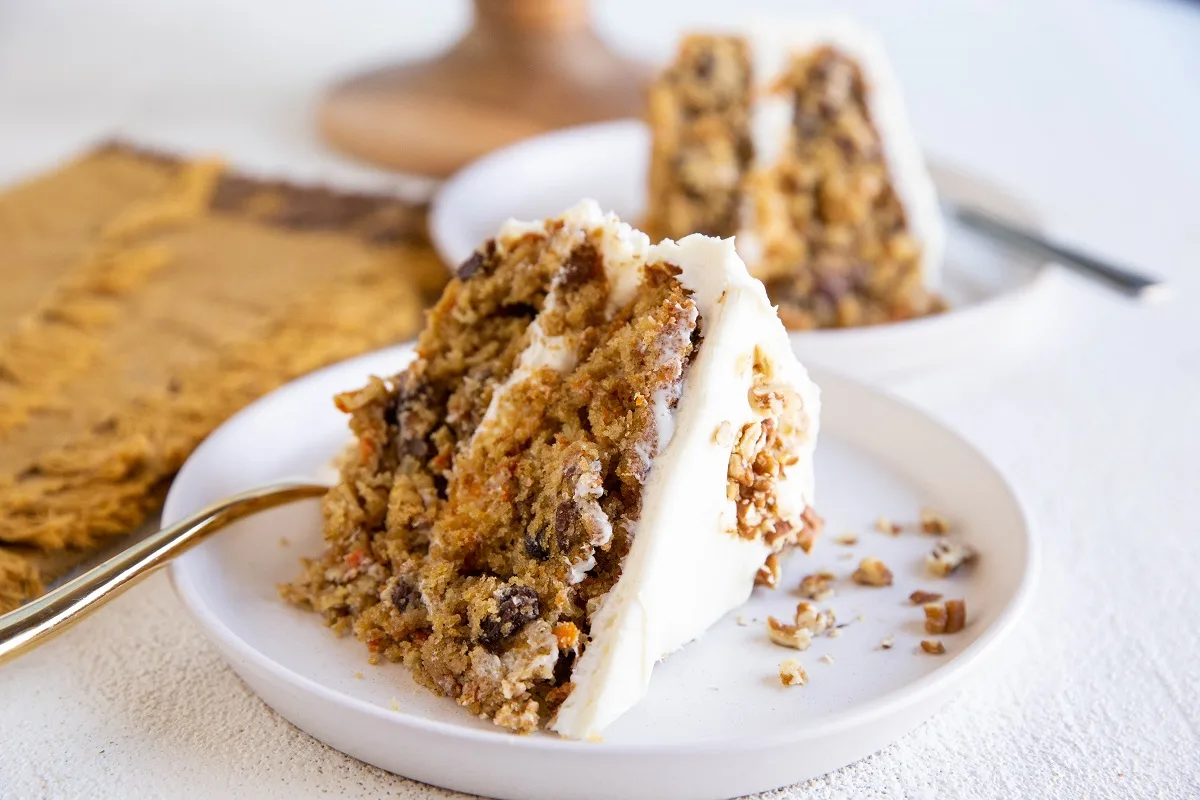 Two slices of carrot cake on white plates with forks, ready to enjoy.