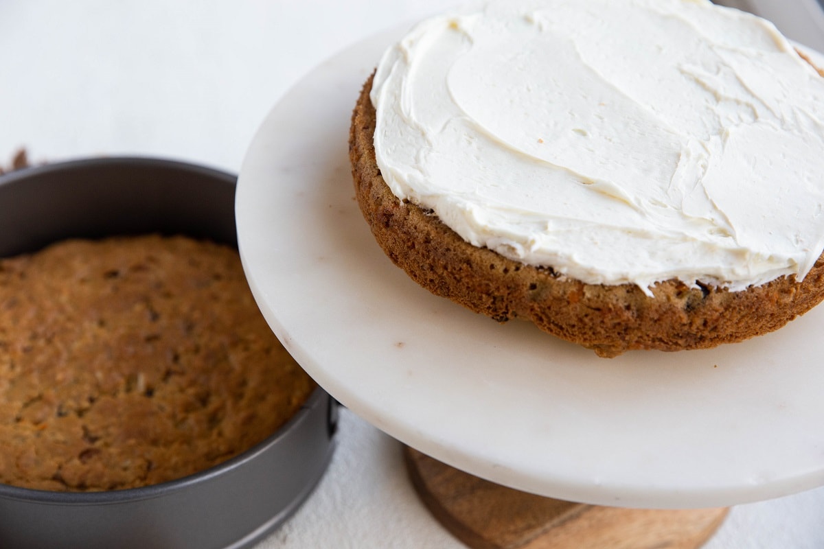 first layer of carrot cake on a cake stand smeared with frosting.