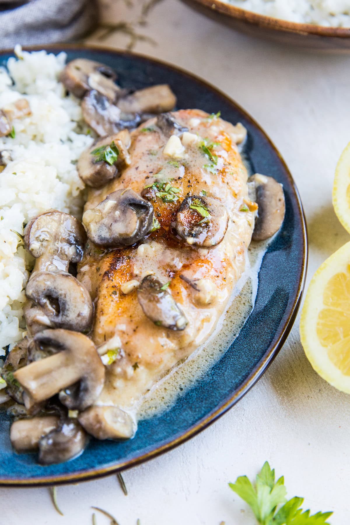 Blue plate with chicken marsala and rice on top and fresh herbs to the side, ready to serve.