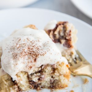Large cinnamon roll with frosting on top with a bite taken out to see the cinnamon swirls on the inside.