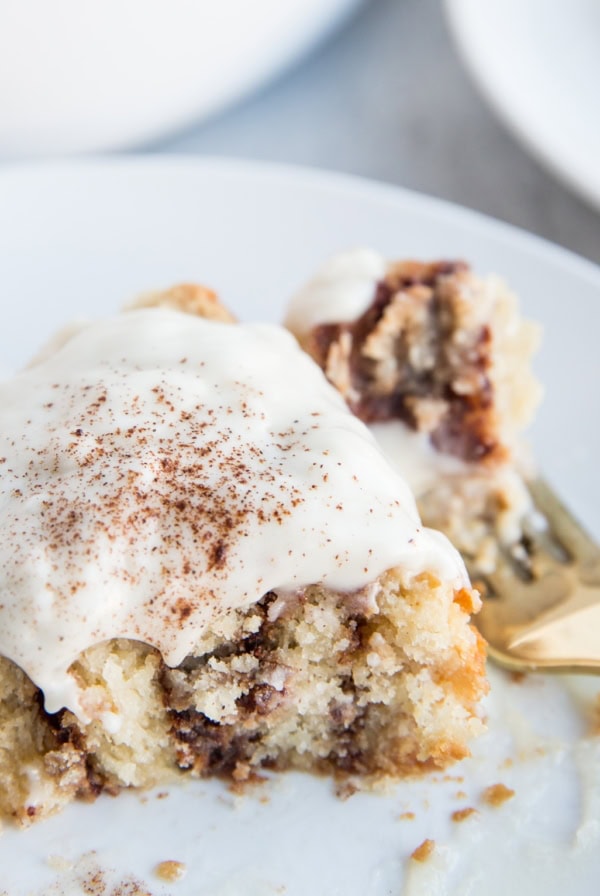 Large cinnamon roll with frosting on top with a bite taken out to see the cinnamon swirls on the inside.