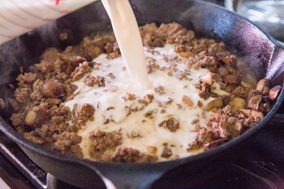 Pouring coconut milk into the skillet with the mushroom meat mixture.