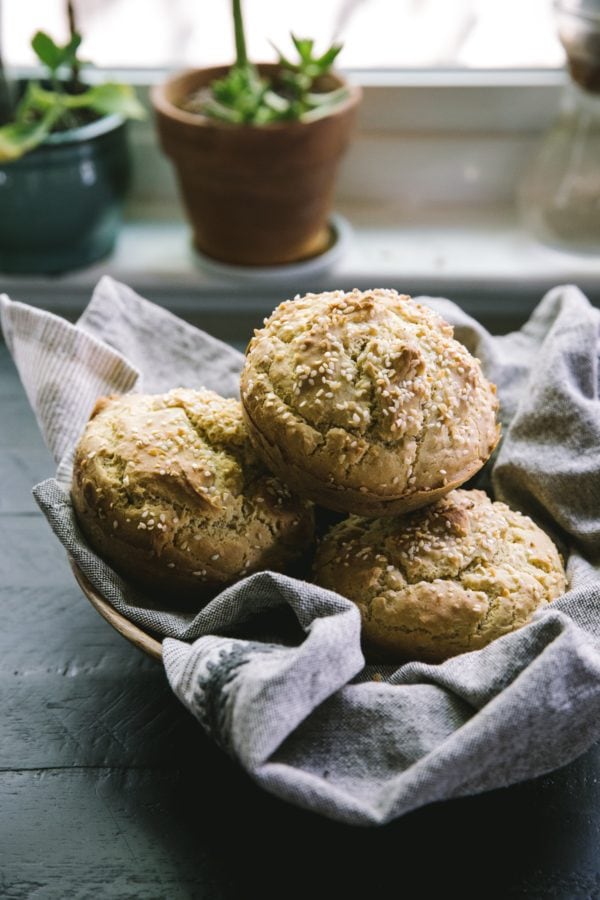 basket of gluten-free hamburger buns sitting on a dark table with plants in the background.