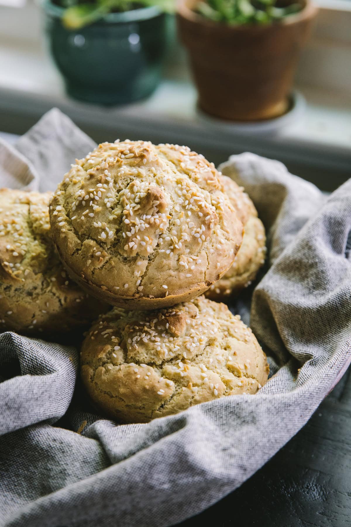 Basket full of gluten-free burger buns wrapped in a cloth napkin with plants in the background.