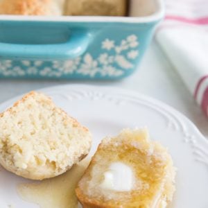 Dairy-Free Gluten-Free Hawaiian Roll on a plate sliced in half and slathered with melted butter and honey with the dish of the rest of the rolls in the background.