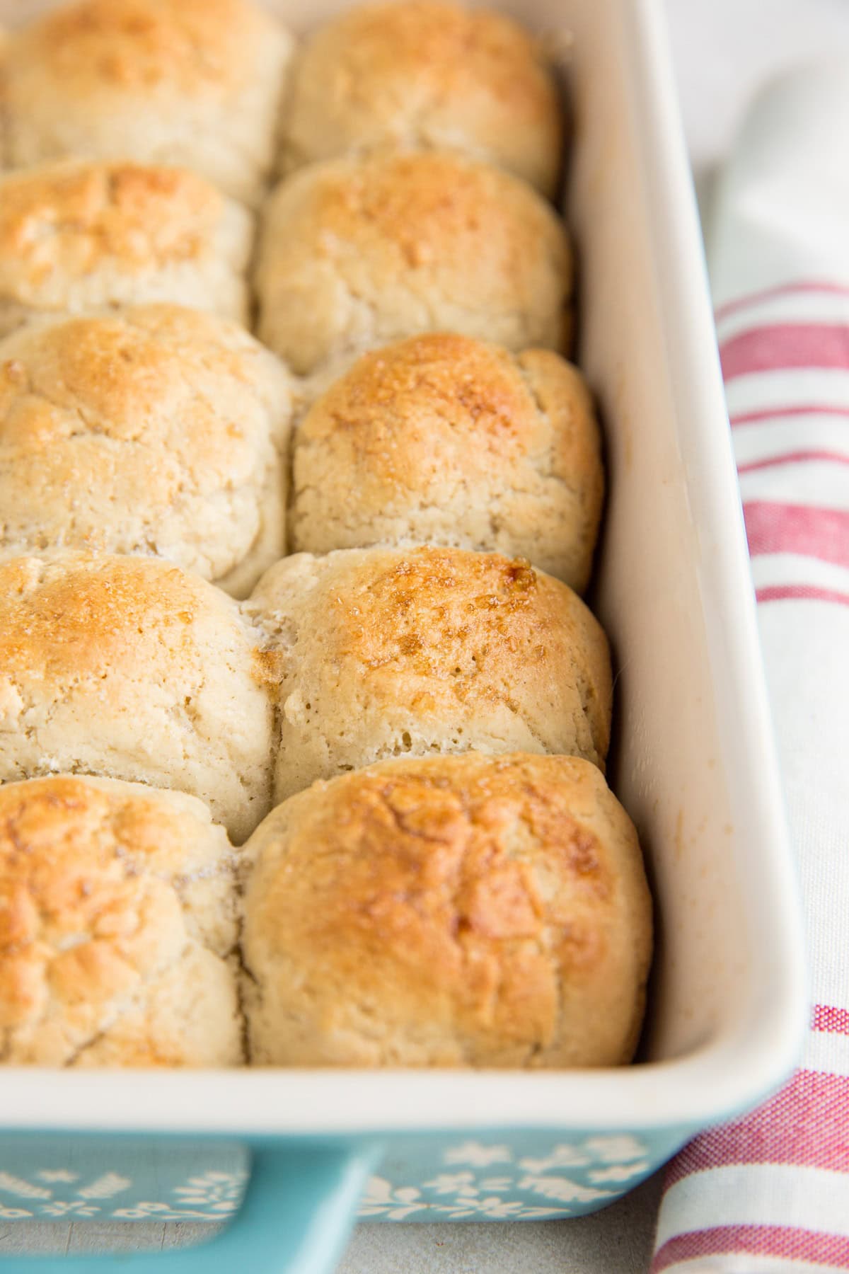 Casserole dish full of golden brown dinner rolls, fresh out of the oven with a red striped napkin to the side.