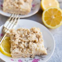 Three decorative plates with roses on them with a lemon crumb bar on top and fork to the side. Fresh lemons in the background.