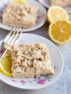 Three decorative plates with roses on them with a lemon crumb bar on top and fork to the side. Fresh lemons in the background.