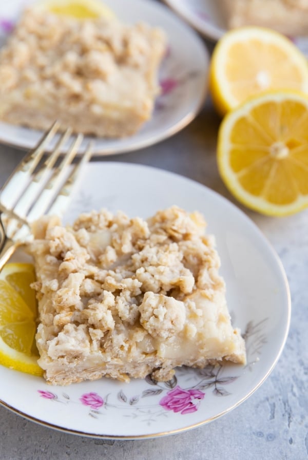 Three decorative plates with roses on them with a lemon crumb bar on top and fork to the side. Fresh lemons in the background.