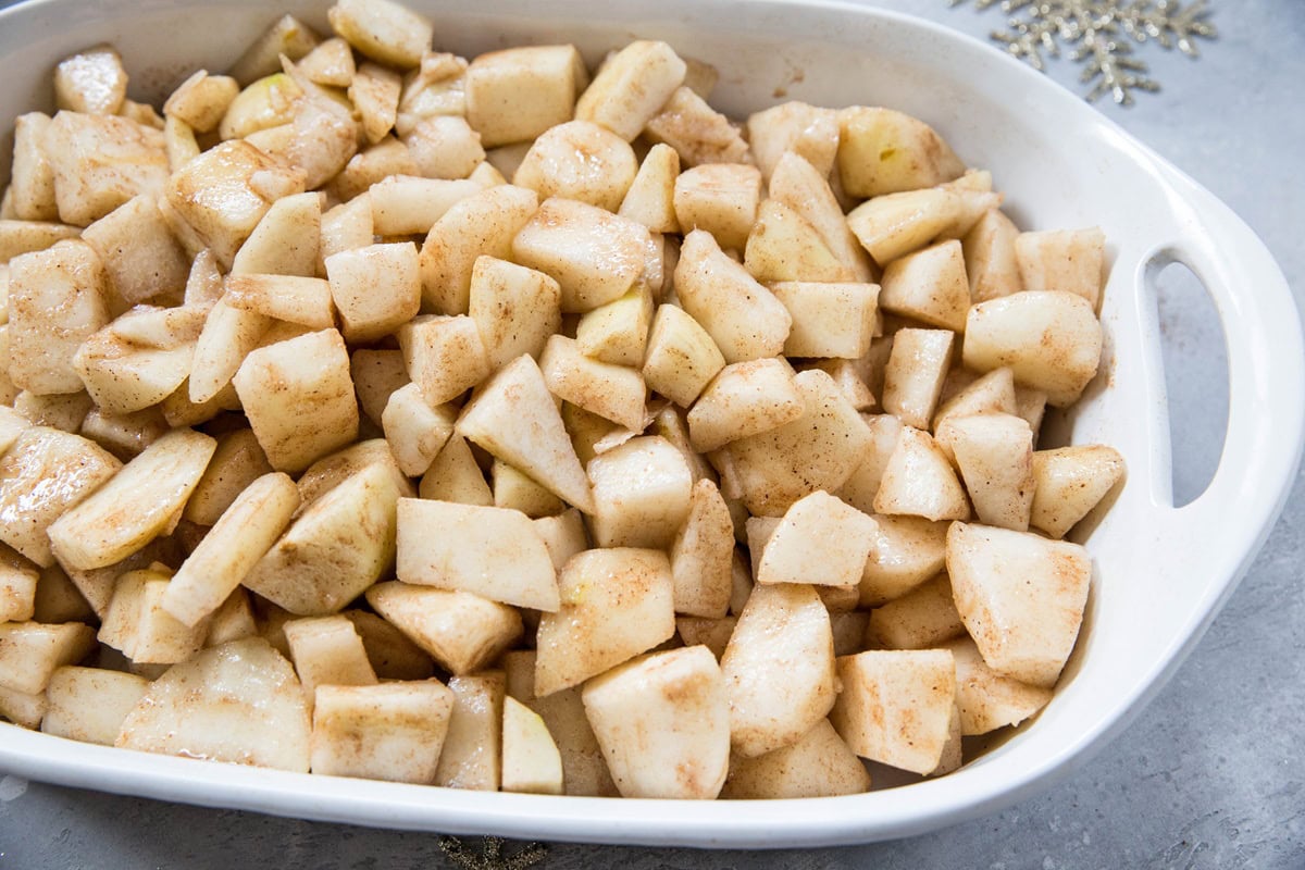 A white baking dish filled with chopped apples coated in cinnamon and sugar, perfect as the base for a gluten-free pear cobbler, ready to be baked.
