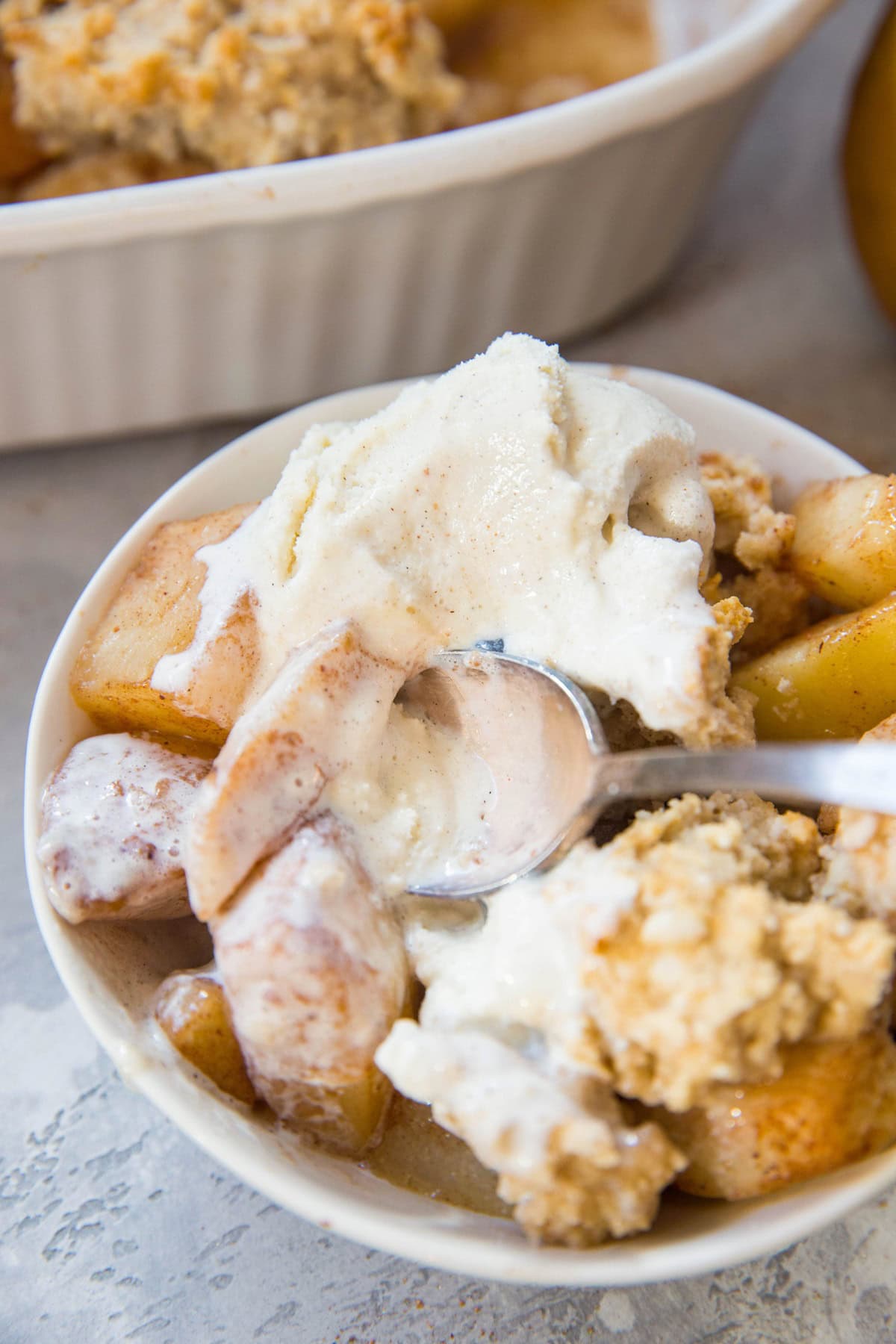 White bowl full of pear cobbler with a scoop of ice cream.
