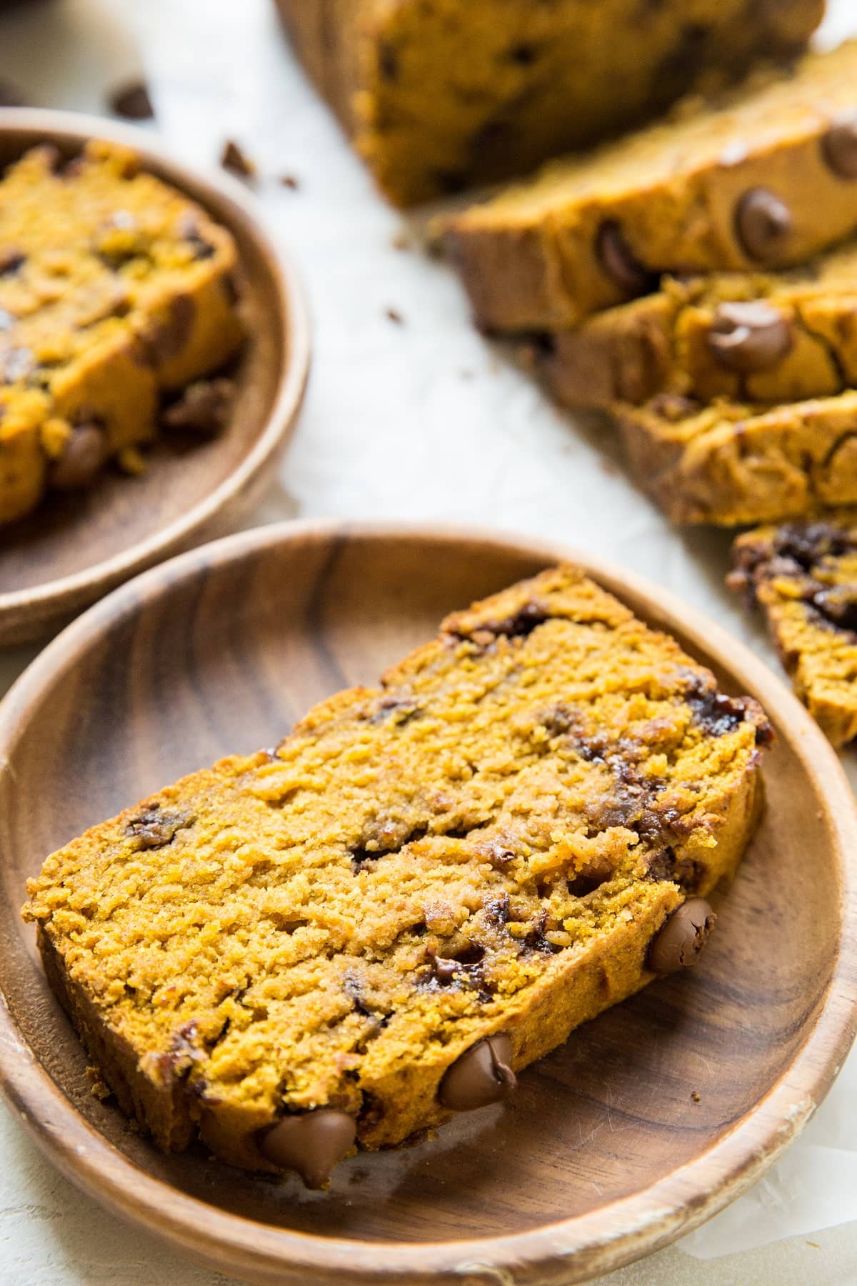 Two slices of pumpkin bread on wooden plates with a loaf of sliced pumpkin bread in the background.