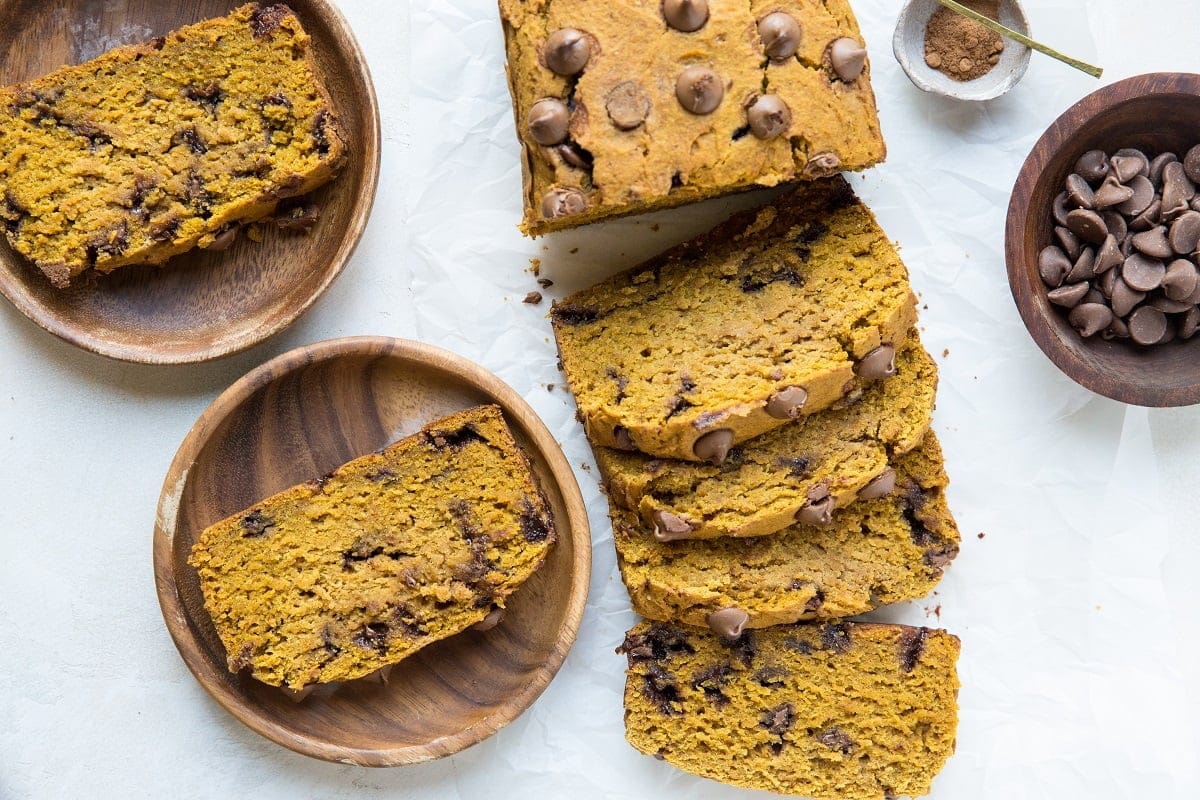 A loaf of gluten-free pumpkin bread sliced into individual slices with slices of bread on plates.