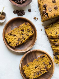 Two wooden plates with slices of pumpkin bread and the rest of the loaf off to the side.