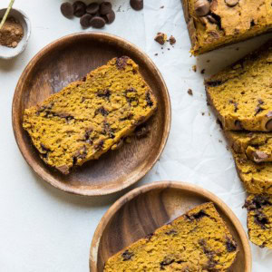 Two wooden plates with slices of pumpkin bread and the rest of the loaf off to the side.