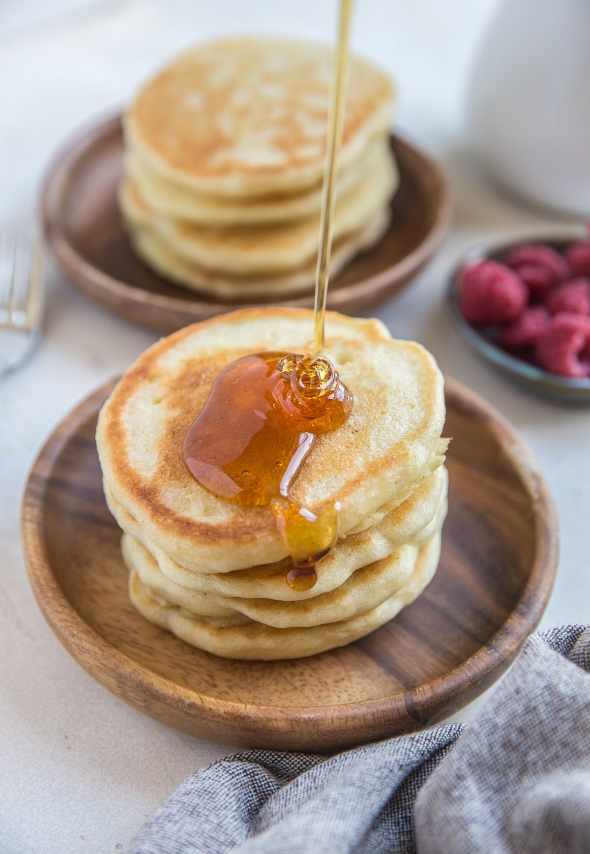 Two plates of sourdough pancakes with syrup being poured on the top of one. Ready to eat!