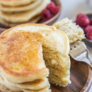 Two wooden plates of Gluten-Free Fluffy Sourdough Pancakes with bite taken out of a stack