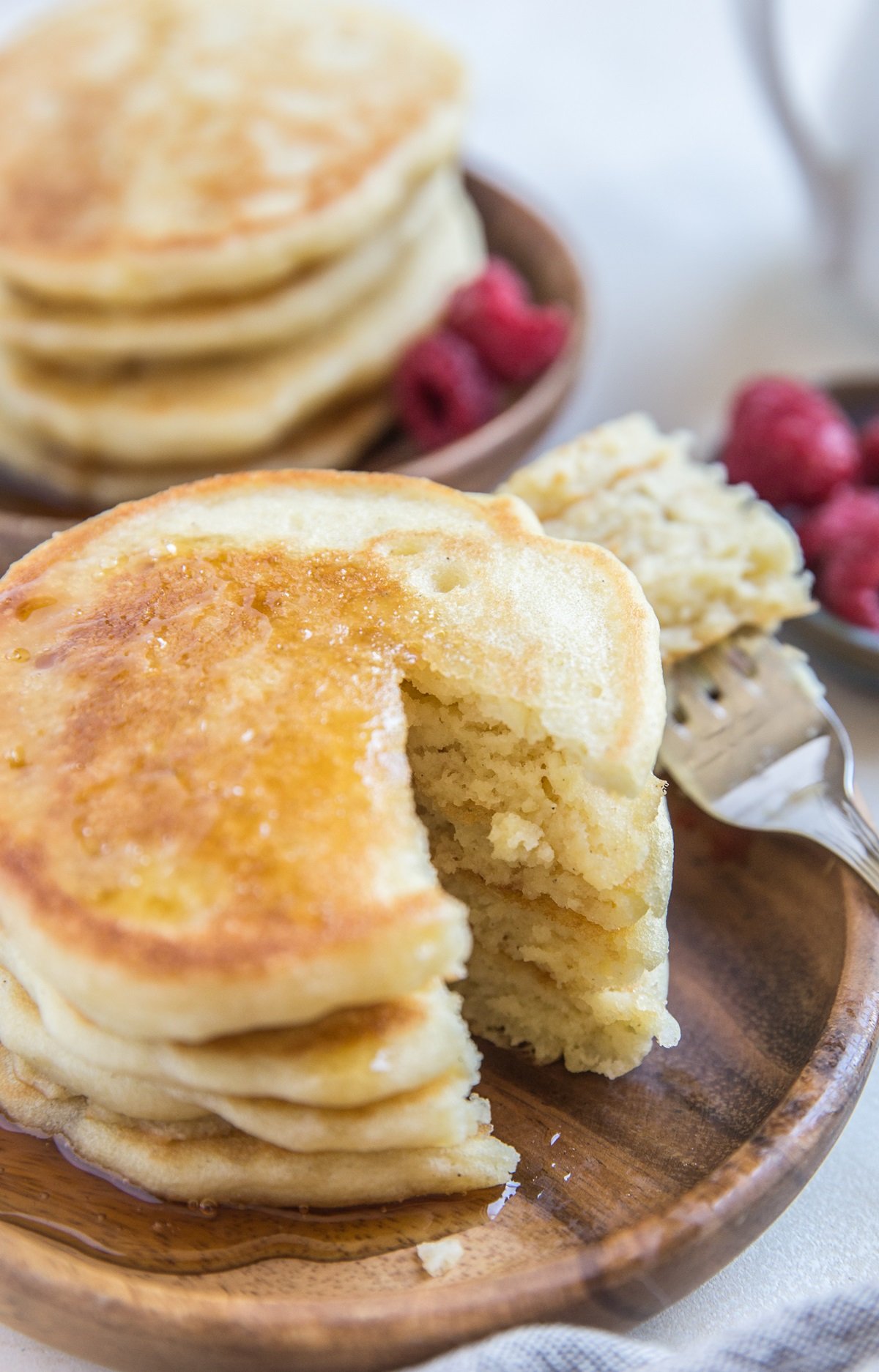 Two wooden plates of Gluten-Free Fluffy Sourdough Pancakes with bite taken out of a stack