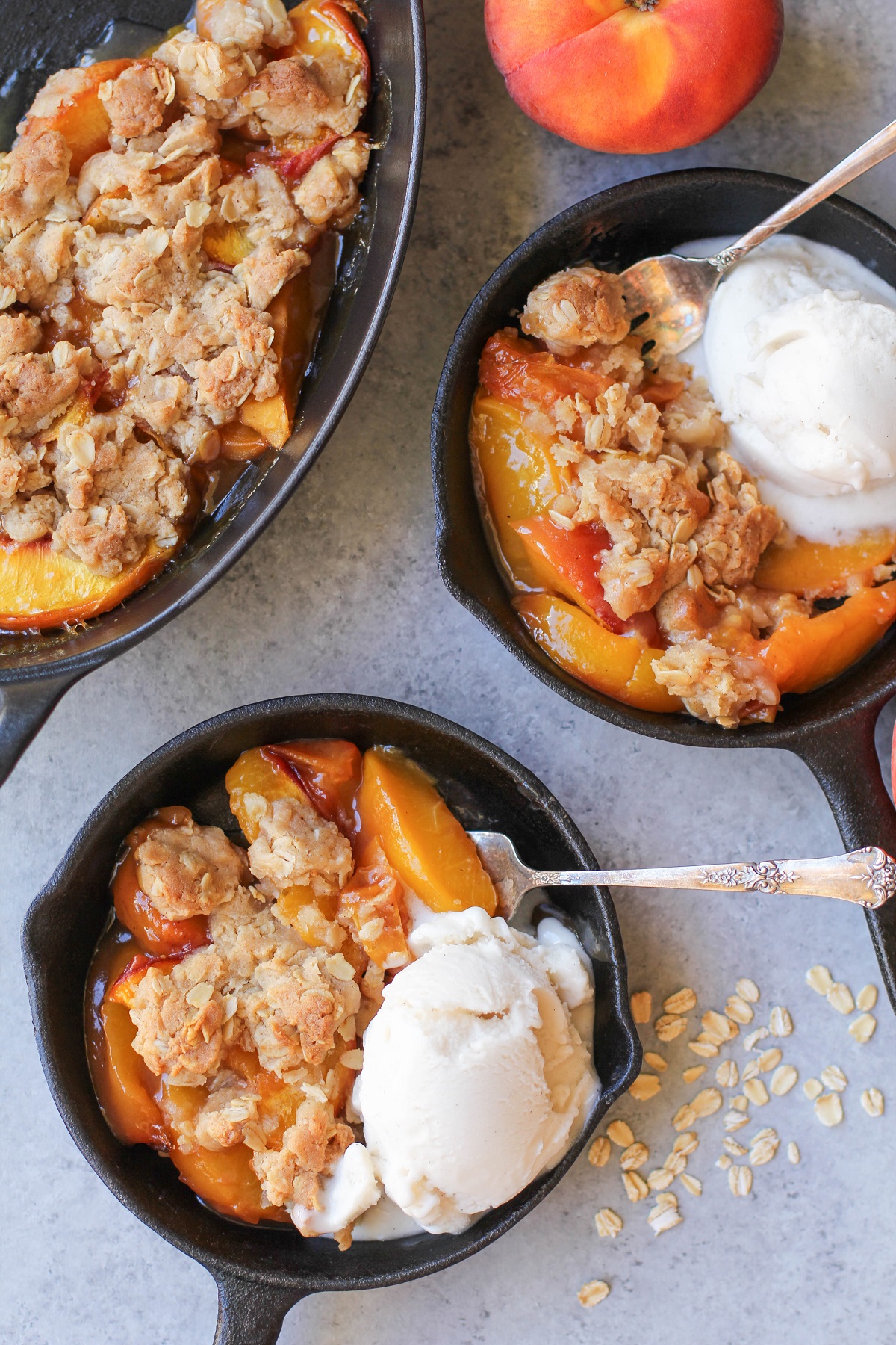 Gluten-Free Vegan Peach Crisp in two small cast iron skillets with scoops of vanilla ice cream, ready to eat.