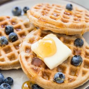 Stack of the best gluten-free waffles on a plate with butter, honey and blueberries